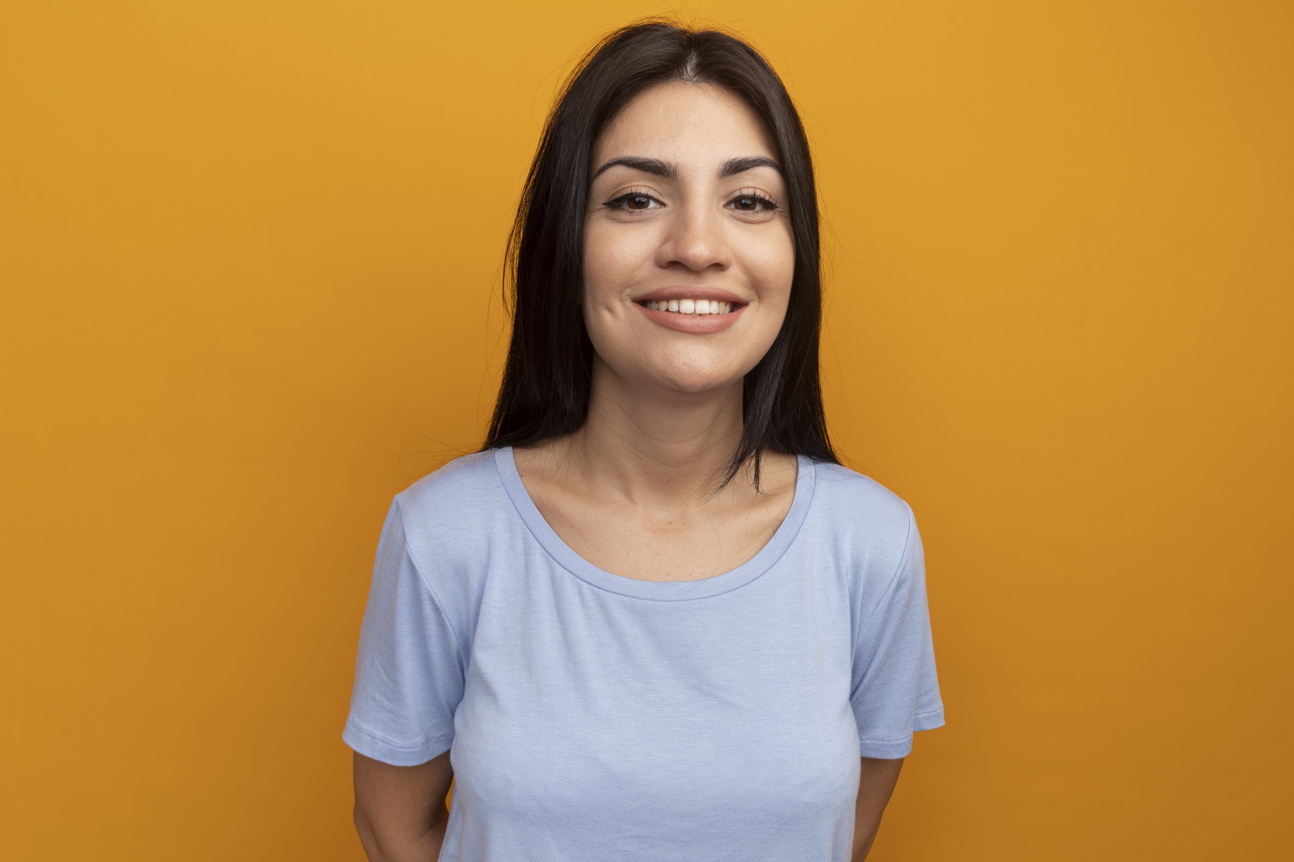 smiling pretty brunette woman looks front isolated orange wall scaled